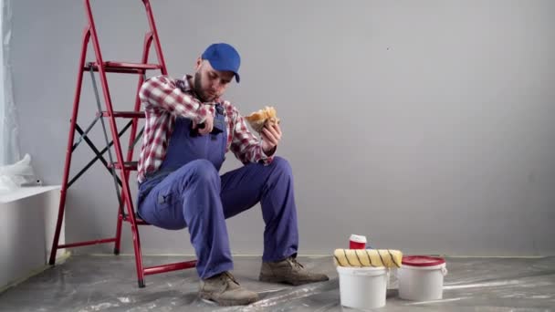 Επισκευές. Βάφω τους τοίχους. Ζωγράφος τρώει ένα burger. Γεύμα στη δουλειά. Τεχνίτης. Αντιγραφή χώρου - Πλάνα, βίντεο