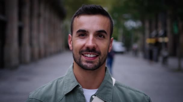 Acercamiento joven barbudo guapo se para mirando a la cámara sonriendo en la calle en la ciudad europea de Barcelona. Alegre posando turista masculino disfruta de ambiente divertido de la experiencia de turismo de viajes al aire libre - Metraje, vídeo