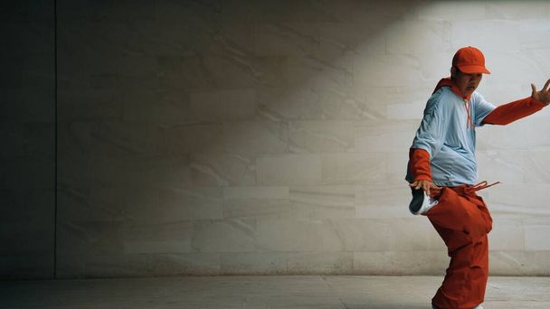 Guapo coreógrafo practicar danza callejera en fondo gris. Joven y atractiva bailarina b boy realizar mientras usa un paño elegante. Sensación de paso animado. Copiar espacio. Deporte al aire libre 2024. Rígidamente.. - Foto, Imagen