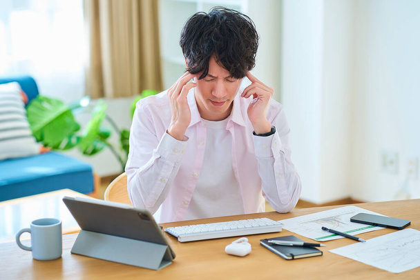 Een jongeman voelt zich gestrest tijdens het bedienen van een computer in zijn kamer - Foto, afbeelding