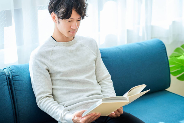 jeune homme lisant un livre dans la chambre - Photo, image