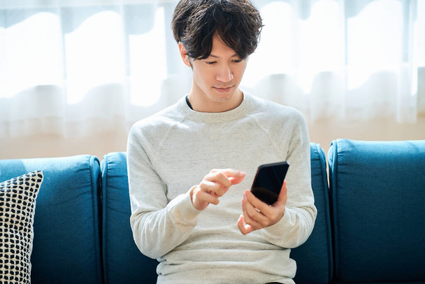 Nuori mies pitelee älypuhelinta sisätiloissa - Valokuva, kuva