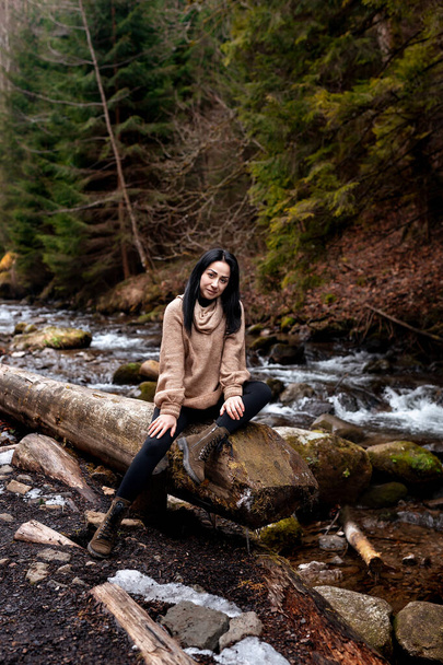 Young brunette woman explores new, magical, and fantastic places around the world. Portrait of cute young female relaxing and smiling in forest with stream - Photo, Image