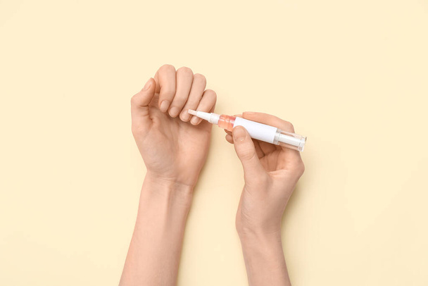 Женские руки наносят кутикулярное масло ручкой на бежевый фон - Фото, изображение