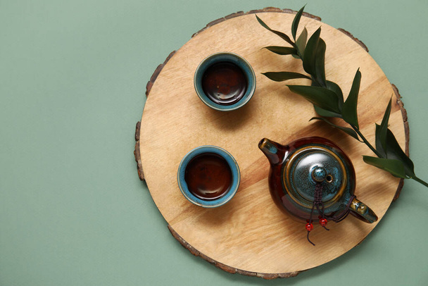 Suporte de madeira com bule de chá, xícaras de chá saboroso e folhas no fundo de azeitona - Foto, Imagem