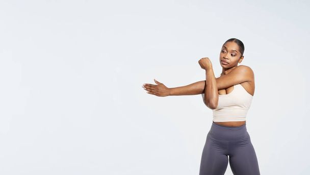 アフリカ系アメリカ人のフィットネスレディーは,ホワイトスタジオの背景をトレーニングする前に腕を伸ばします. アクティブウェアのフィット女性は筋肉を温める. パノラマ,テキストのためのフリースペース - 写真・画像