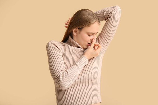 Young woman feeling smell of sweat on beige background. Concept of using deodorant - Foto, afbeelding