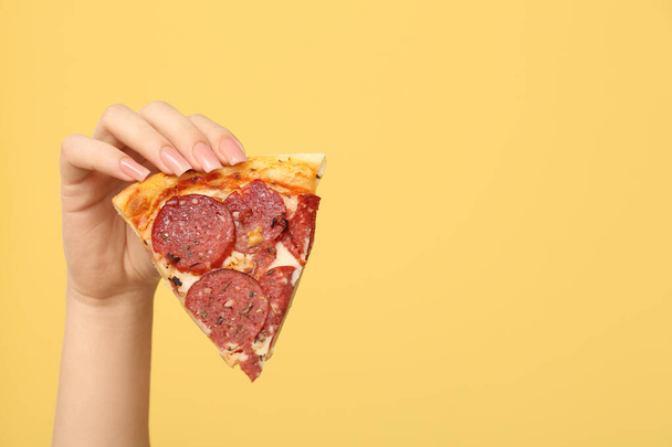 Mano femminile tenendo gustosa fetta di pizza su sfondo giallo - Foto, immagini