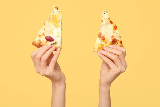 Mains féminines tenant une délicieuse tranche de pizza sur fond jaune - Photo, image