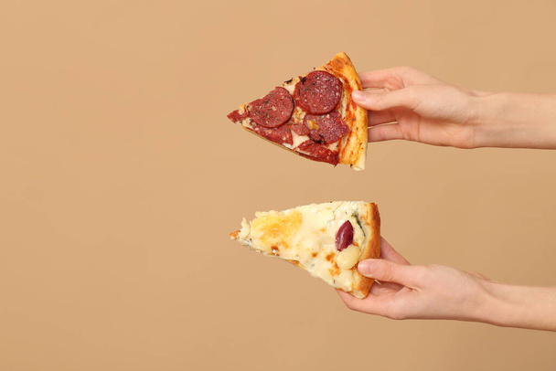 Mani femminili che tengono gustose fette di pizza su sfondo beige - Foto, immagini