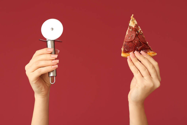Vrouwelijke handen houden pizza slice en pizza cutter op rode achtergrond - Foto, afbeelding
