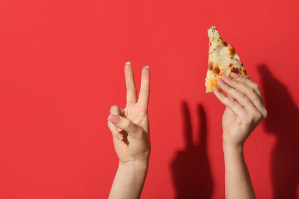 Female hand holding tasty pizza slice and making piece symbol on red background - Photo, Image