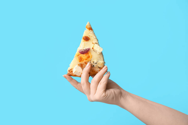 Female hand holding tasty pizza slice on blue background - Fotografie, Obrázek