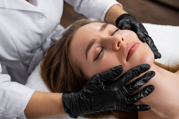 Una hermosa joven se somete a un masaje lifting facial en la clínica de belleza.  - Foto, imagen