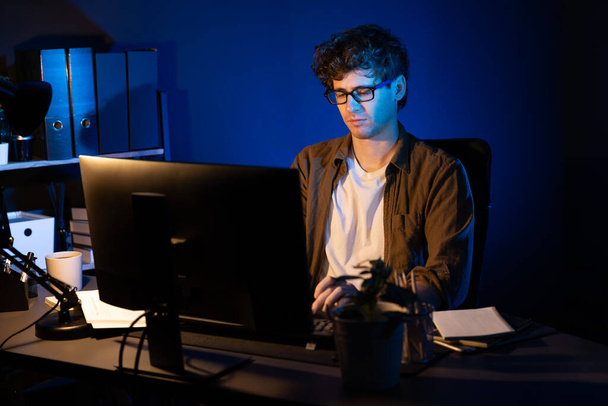 Young businessman concentrating on pc for creative startup project job at neon light modern office. Thinking marketing network online planning of creator to market channel design concept. Gusher. - Photo, Image
