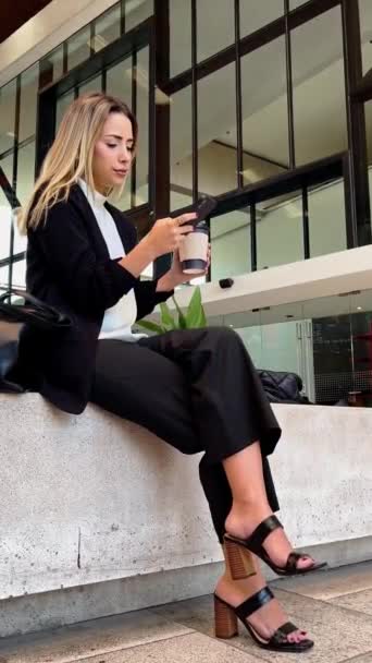 Descanso de café casual en un lugar público moderno: hermosa y relajada rubia latina ejecutiva bebiendo café y usando el teléfono en una plaza pública - Metraje, vídeo