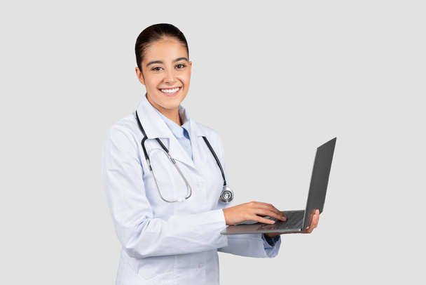 Muhtemelen hasta kayıtları ya da tele sağlık hizmetleri için dizüstü bilgisayar kullanan, omzuna stetoskop takmış profesyonel bir beyaz doktor. - Fotoğraf, Görsel