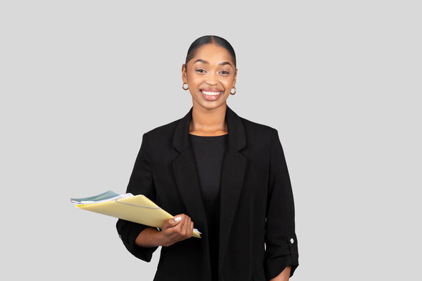 Positive millennial black lady secretary, manager in formal suit documents, clipboard, isolated on gray studio background. Business, work and study, ad and offer, startup - Photo, Image
