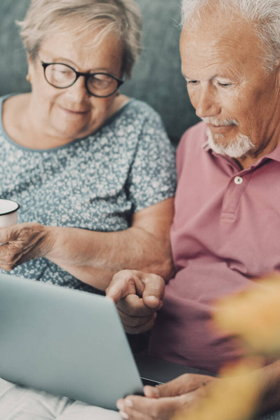 coppia anziana a casa utilizzando il computer portatile e godendo di tempo e attività ricreative al coperto. - Foto, immagini