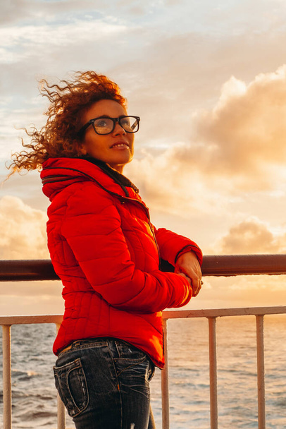 доросла туристична жінка насолоджується теплим помаранчевим заходом сонця на причалі поромного човна під час відпустки. Щасливий мандрівник на океані. Морські хвилі і горизонт на фоні. Подорож пригоди - Фото, зображення