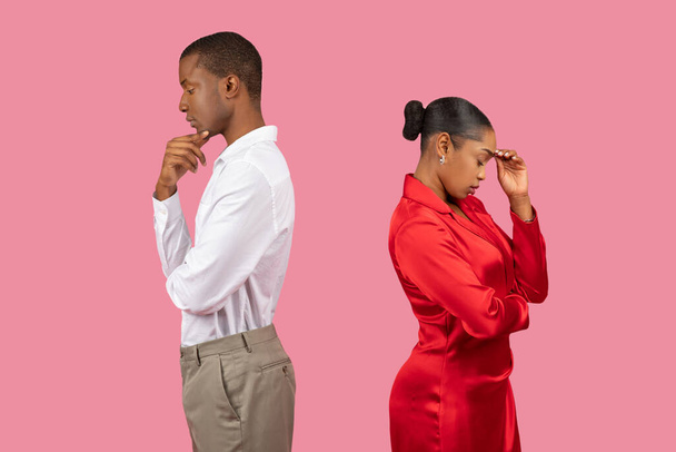 Homme noir réfléchissant et femme contemplative, tous deux debout dos à dos, regardant en bas dans la pensée profonde, isolé sur fond rose, vue de côté - Photo, image