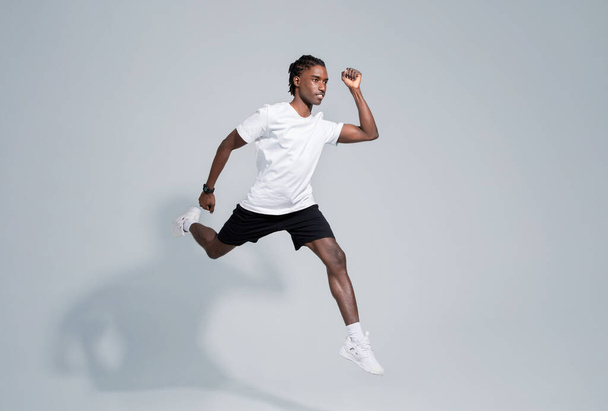 Dynamic black man in sportswear running on grey studio background, in motion shot of motivated young african american male showcasing fitness and active lifestyle, full length, copy space - Photo, Image