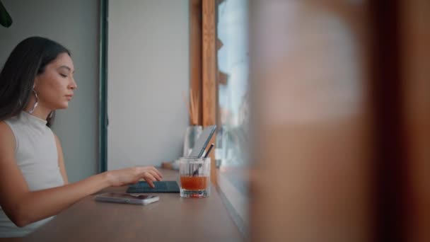 Ázsiai szabadúszó dolgozik cafeteria panoráma ablak közeli. Koncentrált üzletasszony, aki laptopot gépel egyedül a kávézóasztalnál. Gyönyörű lány távoli dolgozó szörfözés internet segítségével étterem wifi. - Felvétel, videó