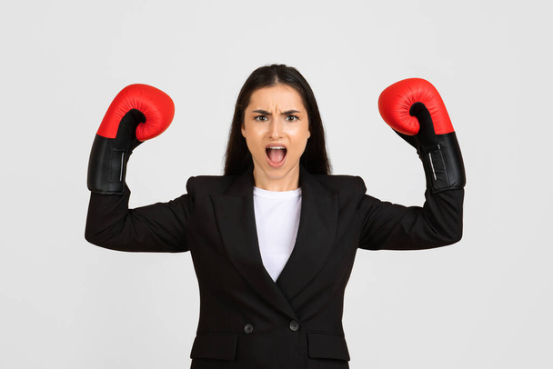 Vurige en krachtige zakenvrouw draagt bokshandschoenen verhoogt haar vuisten in vechtlust, symboliseert uitdaging en kracht in het bedrijfsleven - Foto, afbeelding