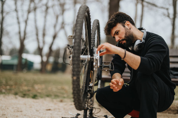 Фокусований підприємець забирає час, щоб виправити і підтримувати свій гірський велосипед на відкритому повітрі в спокійному міському парку. - Фото, зображення