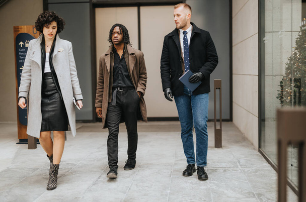Three multiethnic business people in stylish autumn fashion walking confidently together outside a modern office building. - Photo, Image