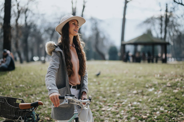 Elegante mujer con bicicleta disfrutando de un día soleado en el parque. - Foto, Imagen