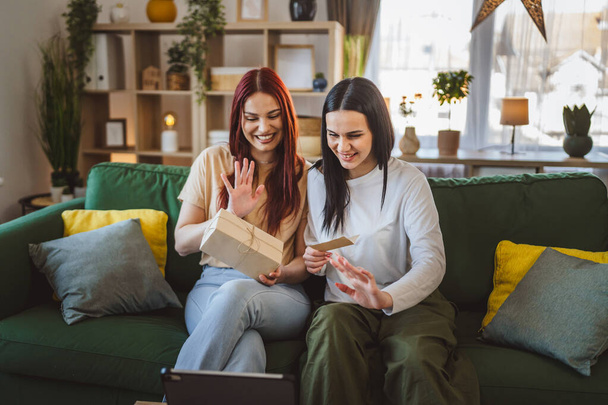 dvě ženy dospívající přátelé nebo sestry dostávají dárky v krabici otevřené čtení karty šťastný úsměv před digitální tablet doma on-line video hovor - Fotografie, Obrázek