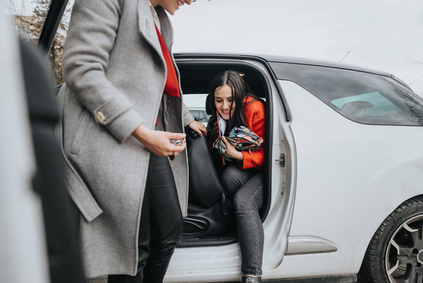 Zwei Geschäftsfrauen lachen miteinander, eine verlässt ein Fahrzeug und die andere steht daneben und symbolisiert eine erfolgreiche Partnerschaft und die Freude an der Teamarbeit im Unternehmensumfeld.. - Foto, Bild