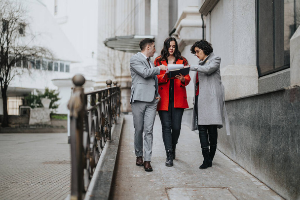 Drei Juristen führen neben einem städtischen Gebäude eine ernsthafte Diskussion, mit Dokumenten in der Hand. - Foto, Bild