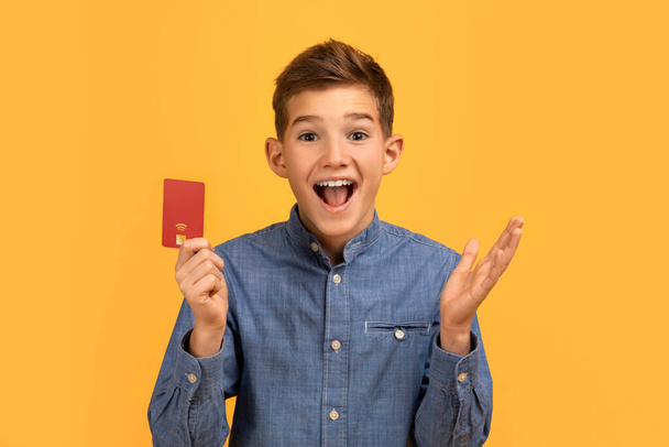 Überrascht Teen Boy mit Kreditkarte und Ausruf vor Freude, glücklich aufgeregt männliche Teenager emotional reagiert auf gute Nachrichten oder Bankangebot, über gelben Studio-Hintergrund stehen, Kopierraum - Foto, Bild