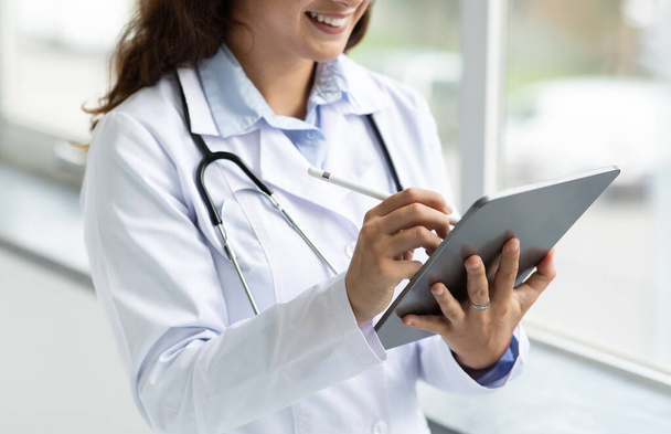 Orvos kezek segítségével digitális tabletta, kivágott női doki van online találkozó a beteg, mellett áll ablak a klinikán. Modern technikusok az egészségügyben - Fotó, kép