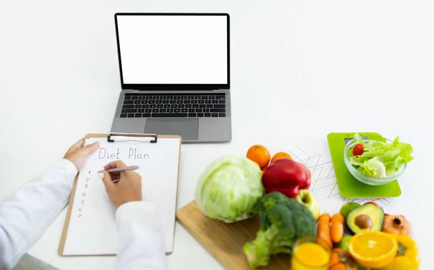 Oříznutá žena lékař nutriční pracuje na notebooku s bílou prázdnou obrazovkou a psaní dietní plán pro pacienta, maketa, kopírovací prostor. Online konzultace s dietologem - Fotografie, Obrázek