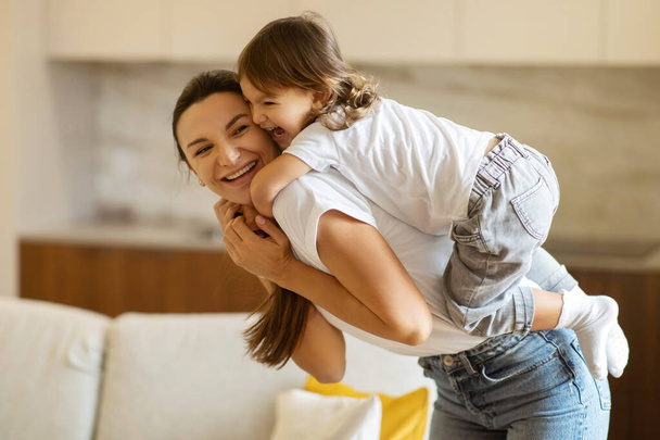 Cheerful Young Mother Riding Adorable Little Daughter On Back, Happy Mom And Preschooler Female Child Laughing And Having Fun Together While Playing In Living Room At Home, Closeup Shot - Photo, Image