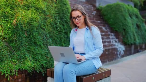 Vrouw zit in het park met laptop en werkt overdag - Video
