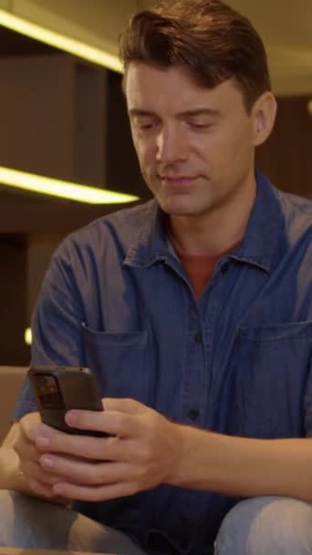 Vertical portrait of smiling Caucasian male entrepreneur using mobile phone and looking at camera - Footage, Video