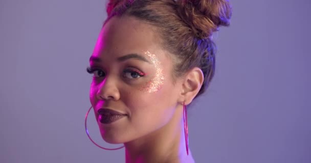 Woman, face and makeup in studio with glitter, earrings and cosmetics with shine by purple background. Girl, model or person with glow, wellness and facial paint with jewelry, sparkle and beauty. - Footage, Video