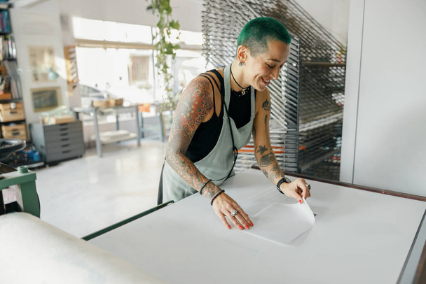 Trabajadora sonriente en delantal preparando película de serigrafía en un taller. Foto de alta calidad - Foto, imagen