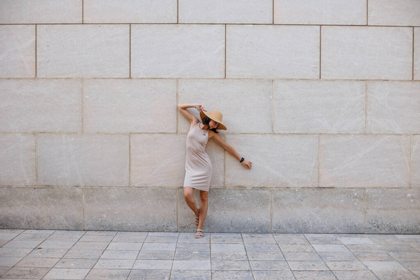 Jeune belle fille souriante dans une robe d'été à la mode. Femme sexy insouciante posant dans la rue contre le mur dans un chapeau. Amusant et rire. - Photo, image