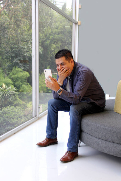 40 éves, sötét bőrű latin férfi az irodájában használja a mobilját, hogy dolgozzon, fizessen, videóhívásokat intézzen, és kedvezményeket és promóciókat találjon. - Fotó, kép