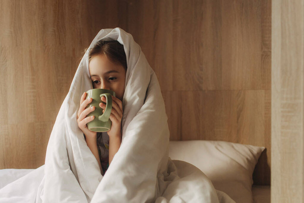 School age girl with cup lies in bed with a respiratory illness at home. Close up photo copy space for text top above view. Pre-teen relaxing in bed bedroom. Health and Medicine concept. - Photo, Image