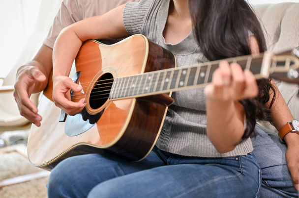 A cropped image of a boyfriend is teaching his girlfriend to play the guitar at home. people and music instrument concepts - Photo, Image