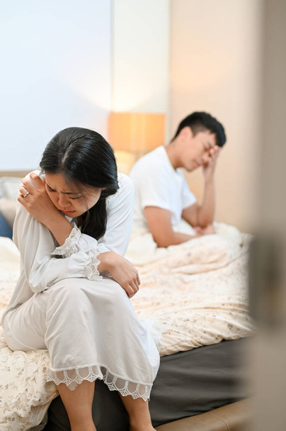 Нещасна, сумна азіатська дружина в піжамі сидить на ліжку, прикриваючи обличчя і плачучи після суперечки з чоловіком. проблеми зі шлюбом, розпад, сварка, нездорові стосунки, розлучення - Фото, зображення