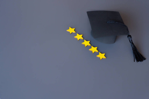 Καπέλο αποφοίτησης δίπλα σε μια σειρά από πέντε αστέρια βαθμολογία σε ένα γκρι φόντο. Αντιγραφή χώρου για κείμενο. Έννοια του συστήματος καλύτερης εκπαίδευσης. - Φωτογραφία, εικόνα