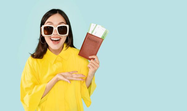 Time For Vacation. Excited Brunette Young Woman Holding Passport And Plane Boarding Pass Tickets, Ready For Trip, Wearing Sunglasses, Isolated On Blue Studio Wall, Banner, Copy Space - Photo, Image