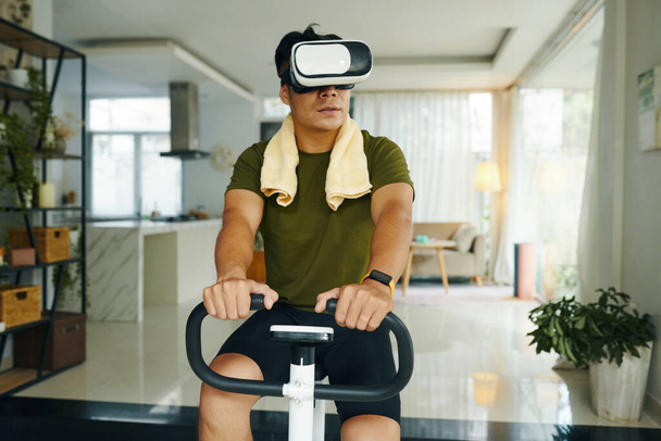 Retrato de homem apto vestindo capacete vr quando sentado em bicicleta de exercício - Foto, Imagem